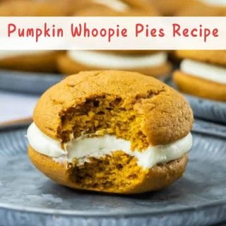 A pumpkin whoopie pie with a bite taken out, filled with white cream, sits on a gray plate with more whoopie pies blurred in the background.