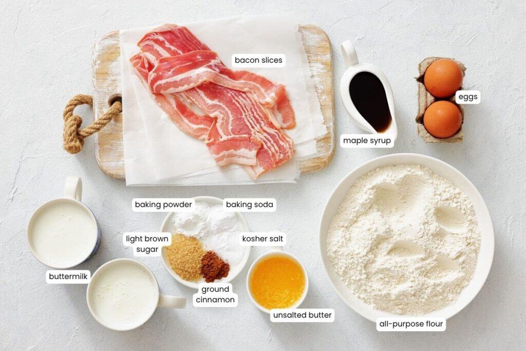 Top-down view of various labeled pancake ingredients, including bacon, eggs, maple syrup, flour, butter, buttermilk, sugars, cinnamon, baking powder, baking soda, and salt.