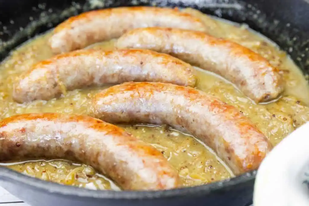Five browned sausages cooking in a skillet with a thick onion gravy.
