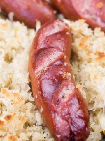 Close-up of browned sausages on a bed of sauerkraut and breadcrumbs in a baking dish.