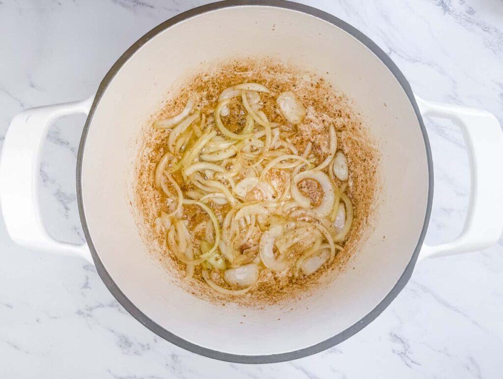 Sliced onions are being saut&eacute;ed in a large white pot, with some browning visible on the bottom surface.