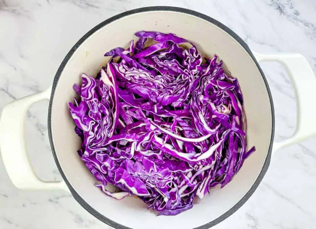 Sliced red cabbage in a white pot on a marble countertop, ready for cooking.