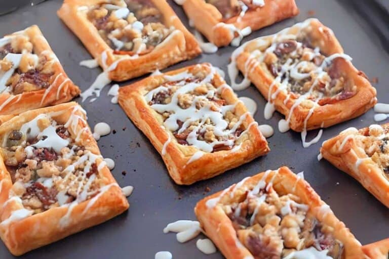 Rectangular puff pastries topped with a crumble and white icing are arranged on a dark baking sheet.