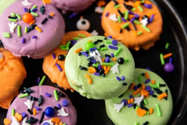 Colorful cookies coated in purple, orange, and green icing, topped with assorted Halloween-themed sprinkles on a black plate.