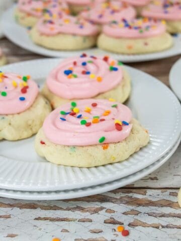 Pink frosted sugar cookies on white plates.