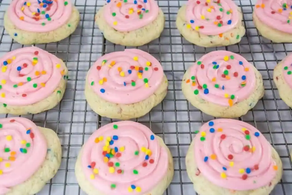 Pink frosted sugar cookies on a cooling rack.