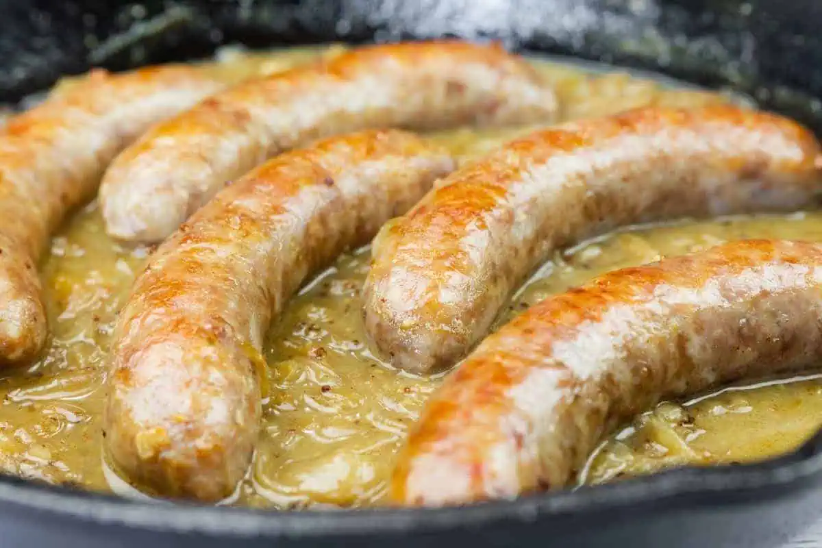 Five Beer Braised Bratwurst cooking in a skillet with a thick, light brown gravy or sauce.