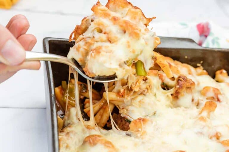A hand lifts a serving of meatball casserole from a rectangular baking dish, showing melted cheese stretching.