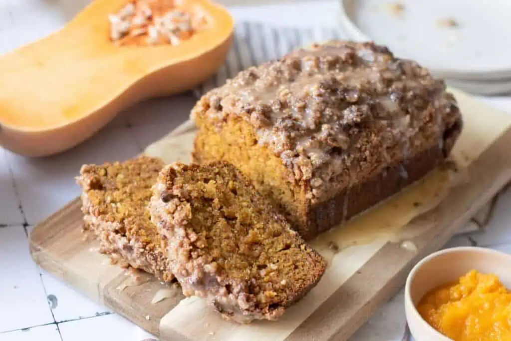A loaf of Pumpkin Bread with Streusel & Glaze sits on a cutting board, with two slices cut.