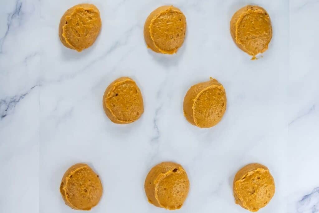 Raw pumpkin whoopie pie batter scooped into rounds on parchment paper, ready for baking.