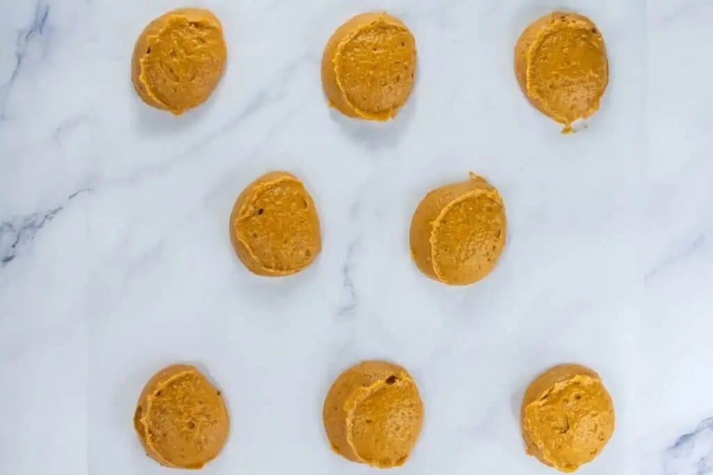 Raw pumpkin whoopie pie batter scooped into rounds on parchment paper, ready for baking.