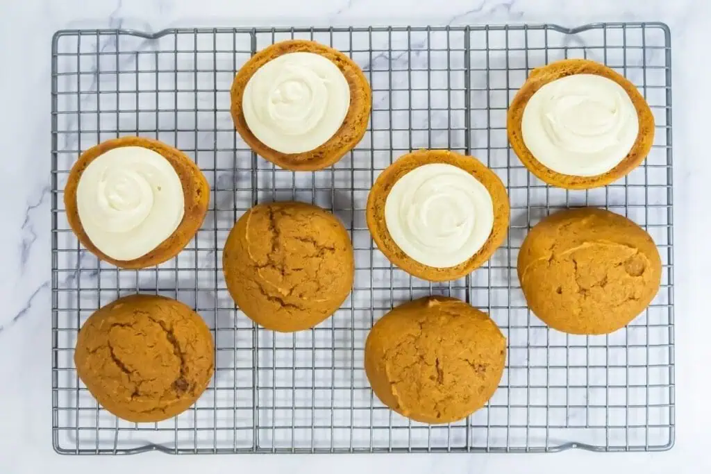 Pumpkin whoopie pie halves on a cooling rack, some topped with cream filling and others plain.