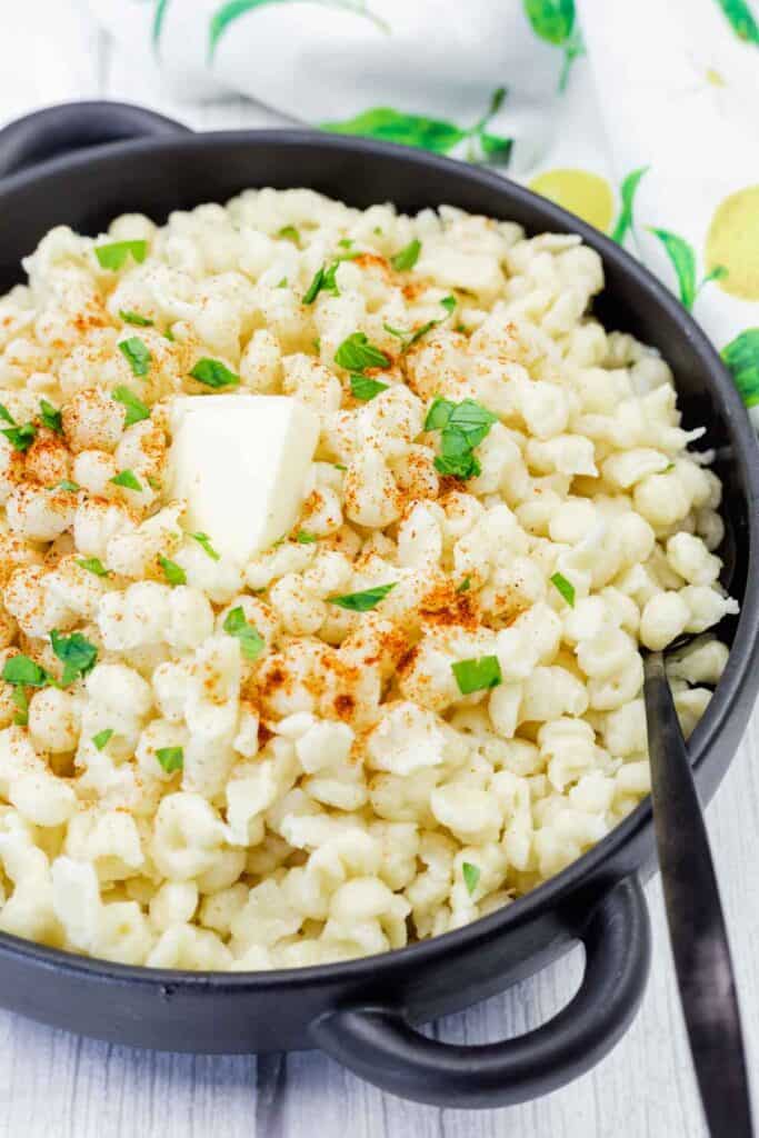 A black dish with a Spaetzle on a white wooden table.