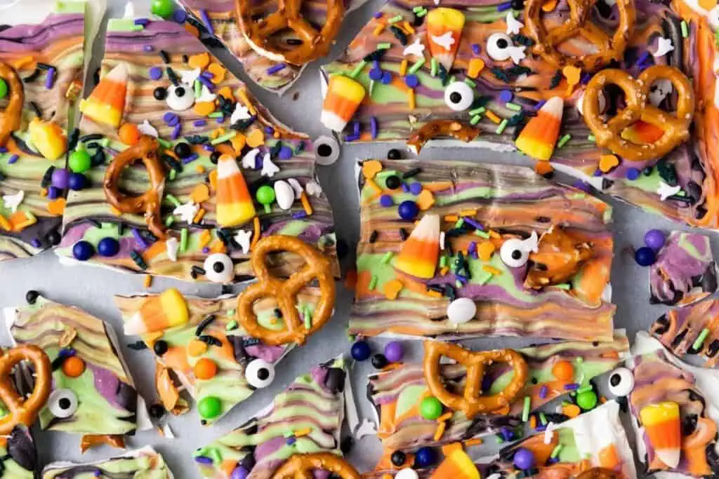 Halloween-themed chocolate bark topped with pretzels, candy corn, candy eyeballs, and colorful sprinkles, broken into irregular pieces.