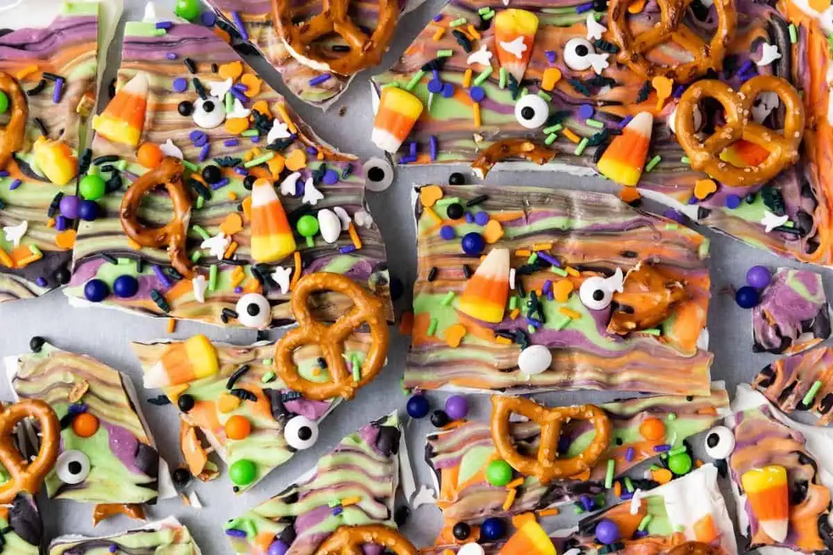 Halloween-themed chocolate bark topped with pretzels, candy corn, candy eyeballs, and colorful sprinkles, broken into irregular pieces.