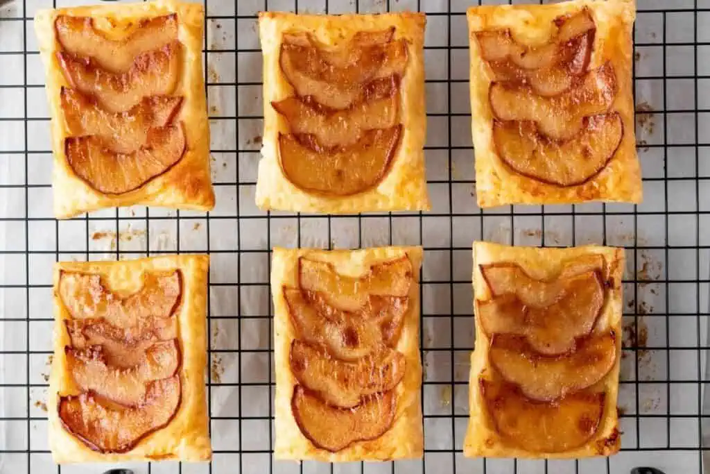Six rectangular apple tarts with caramelized apple slices on puff pastry, arranged on a cooling rack.