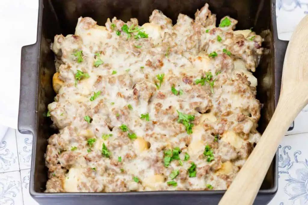 A casserole dish filled with a baked mixture of ground meat, cheese, and chopped parsley, with a wooden spoon on the side.