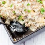 A baking dish with a creamy casserole topped with ground meat and chopped parsley; a spoon rests in one corner, showing a serving removed.