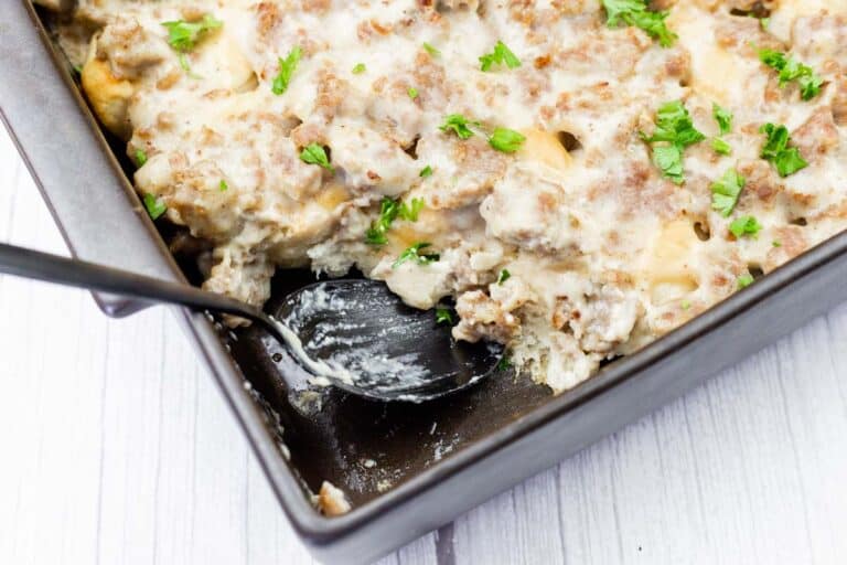 A baking dish with a creamy casserole topped with ground meat and chopped parsley; a spoon rests in one corner, showing a serving removed.
