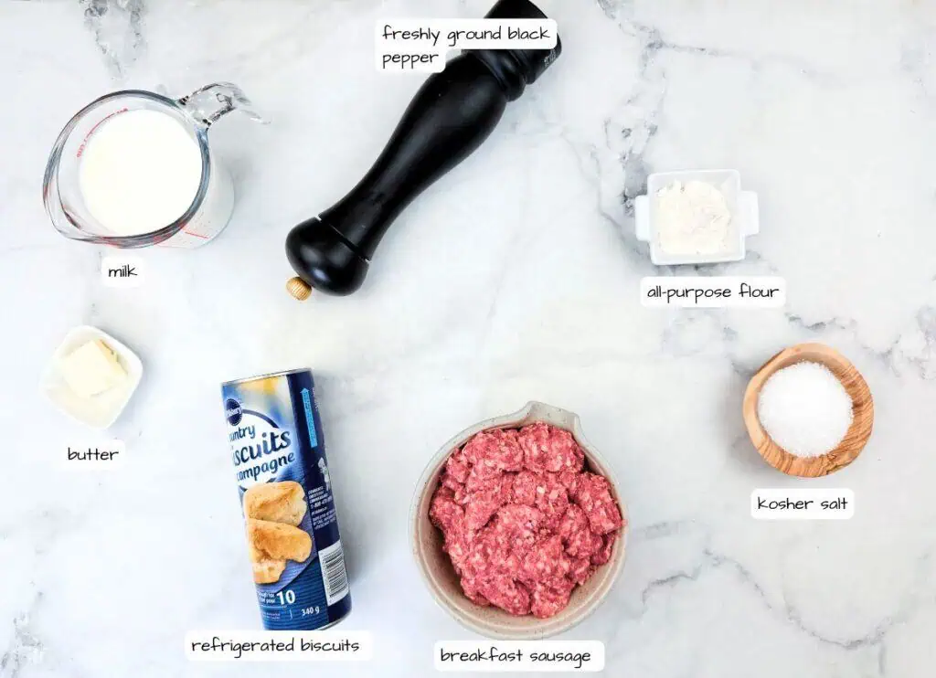 Ingredients for biscuits and gravy laid out on a counter: milk, butter, refrigerated biscuits, breakfast sausage, flour, black pepper, and kosher salt.