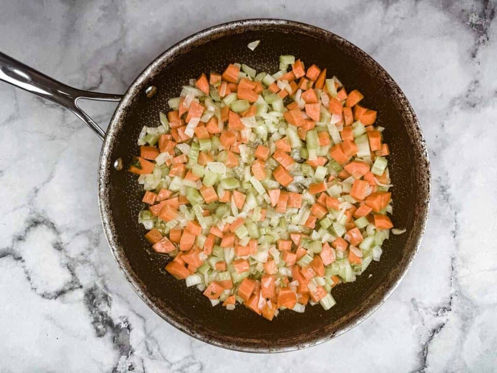 Pan with diced carrots, celery, and onions saut&eacute;ing on a marble countertop.