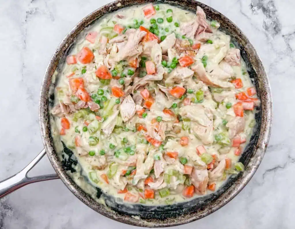 A skillet filled with creamy chicken, peas, carrots, and celery mixture on a marble surface.