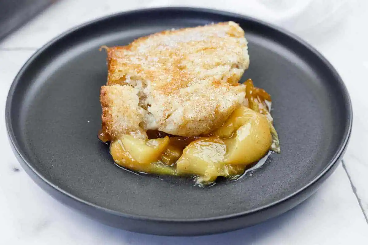 A serving of peach cobbler with a golden crust and peach filling on a black plate.