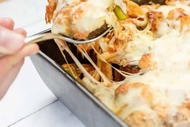 A hand uses a spoon to serve Easy Cheesy Meatball Casserole from a rectangular baking dish, with melted cheese stretching from the dish.