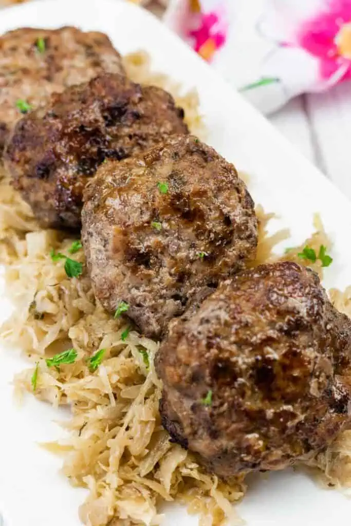Four browned meat patties are served on a bed of shredded cabbage, garnished with chopped parsley, on a white rectangular plate.