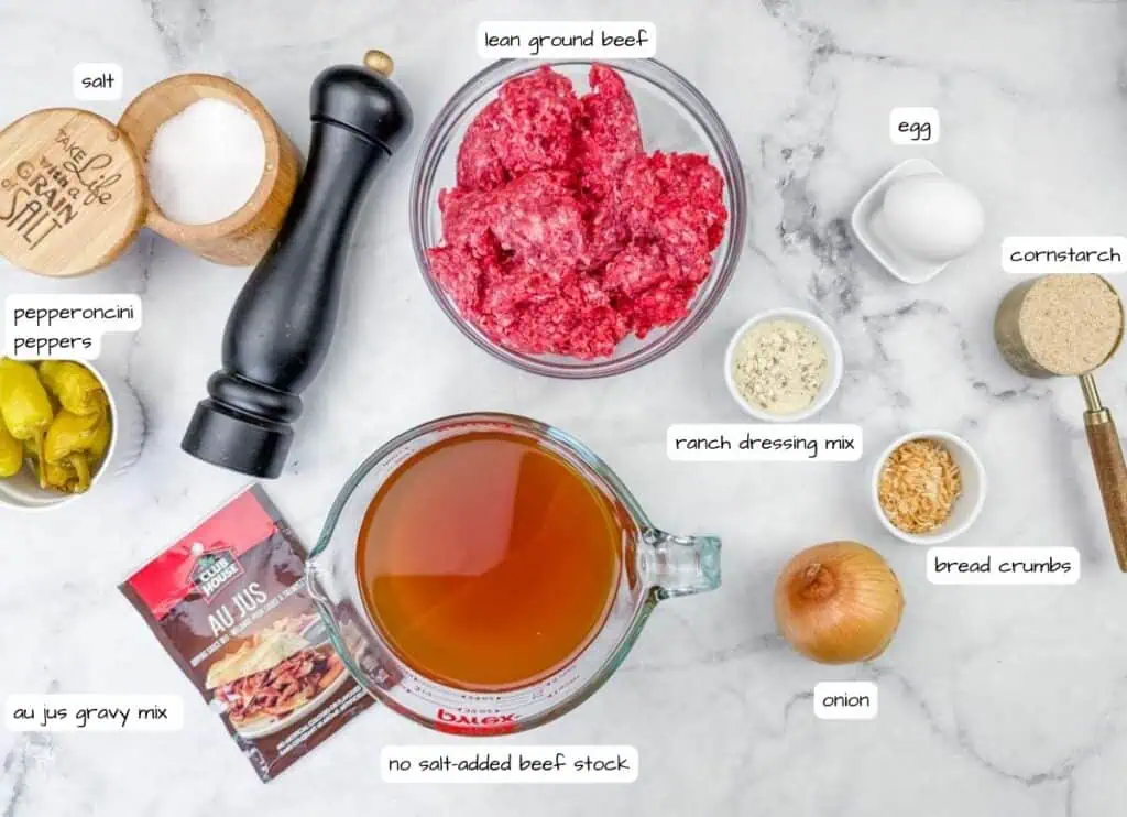 Ingredients for a beef recipe laid out on a countertop: ground beef, egg, cornstarch, bread crumbs, onion, au jus mix, beef stock, pepperoncini peppers, salt, pepper, and ranch dressing mix.