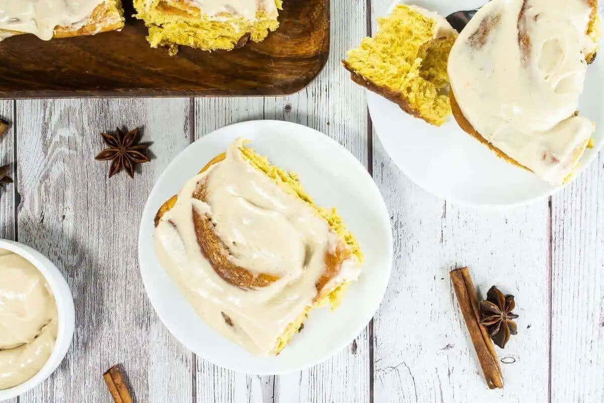 Homemade cinnamon rolls with cream cheese frosting on wooden serving board.
