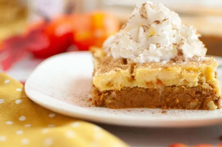 A slice of layered pumpkin dessert topped with whipped cream and sprinkled with cinnamon, served on a white plate.
