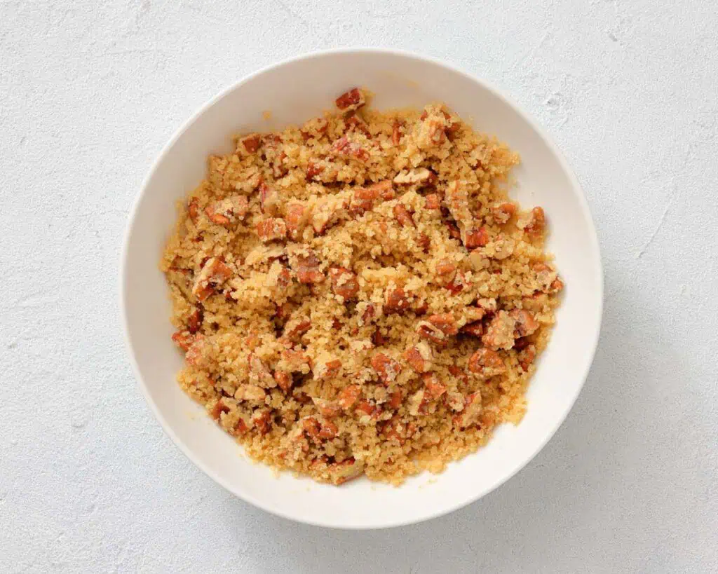 A white bowl filled with crumbled bacon mixed with golden brown breadcrumbs on a light surface.