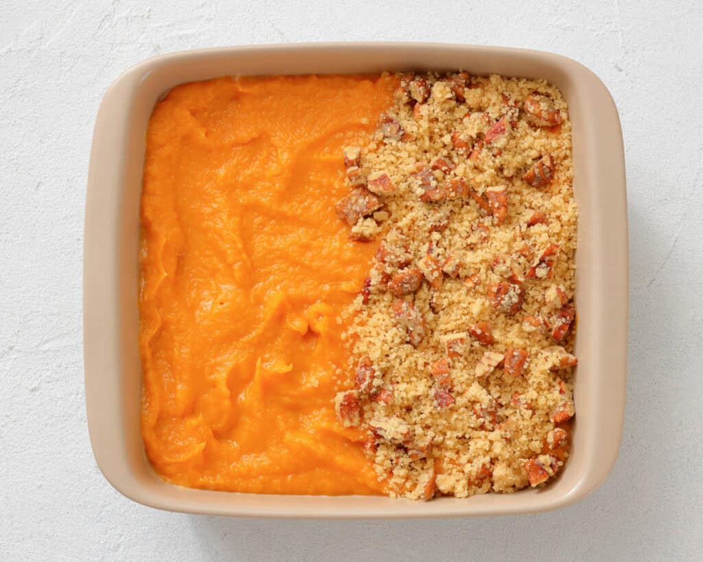 Square baking dish with half covered in smooth orange sweet potato puree and the other half topped with a crumbly pecan streusel topping.