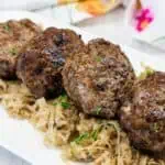 Four browned meat patties are served on a bed of shredded cabbage on a white plate.