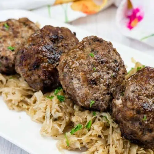 Four browned meat patties are served on a bed of shredded cabbage on a white plate.