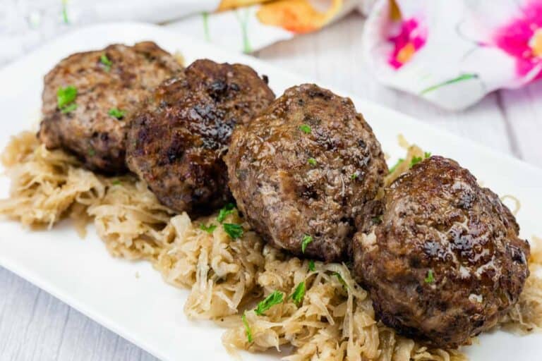 Four browned meat patties are served on a bed of shredded cabbage on a white plate.