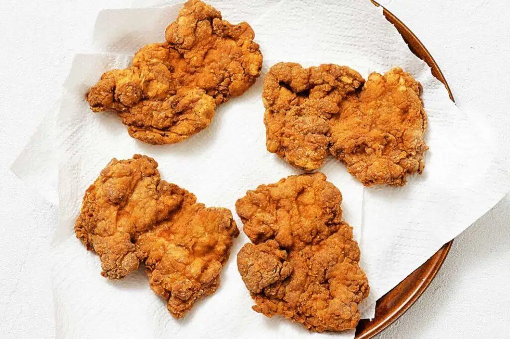 Five pieces of golden-brown fried chicken on a plate lined with white paper towels.