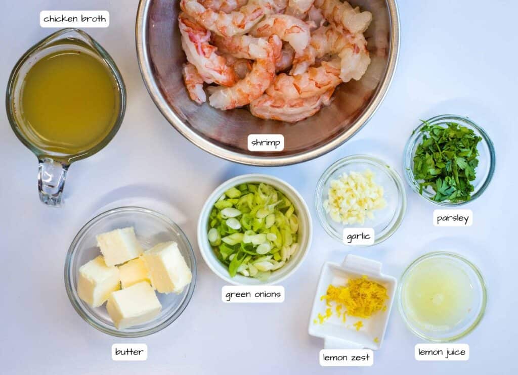 A top-down view of shrimp in a metal bowl, surrounded by small bowls containing chicken broth, butter, green onions, garlic, parsley, lemon zest, and lemon juice, all labeled.