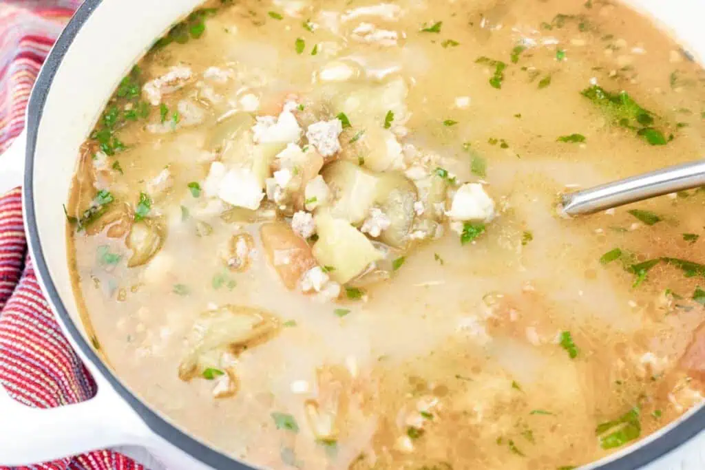 A pot of soup containing ground meat, chopped vegetables, herbs, and a clear broth, with a metal ladle inside.