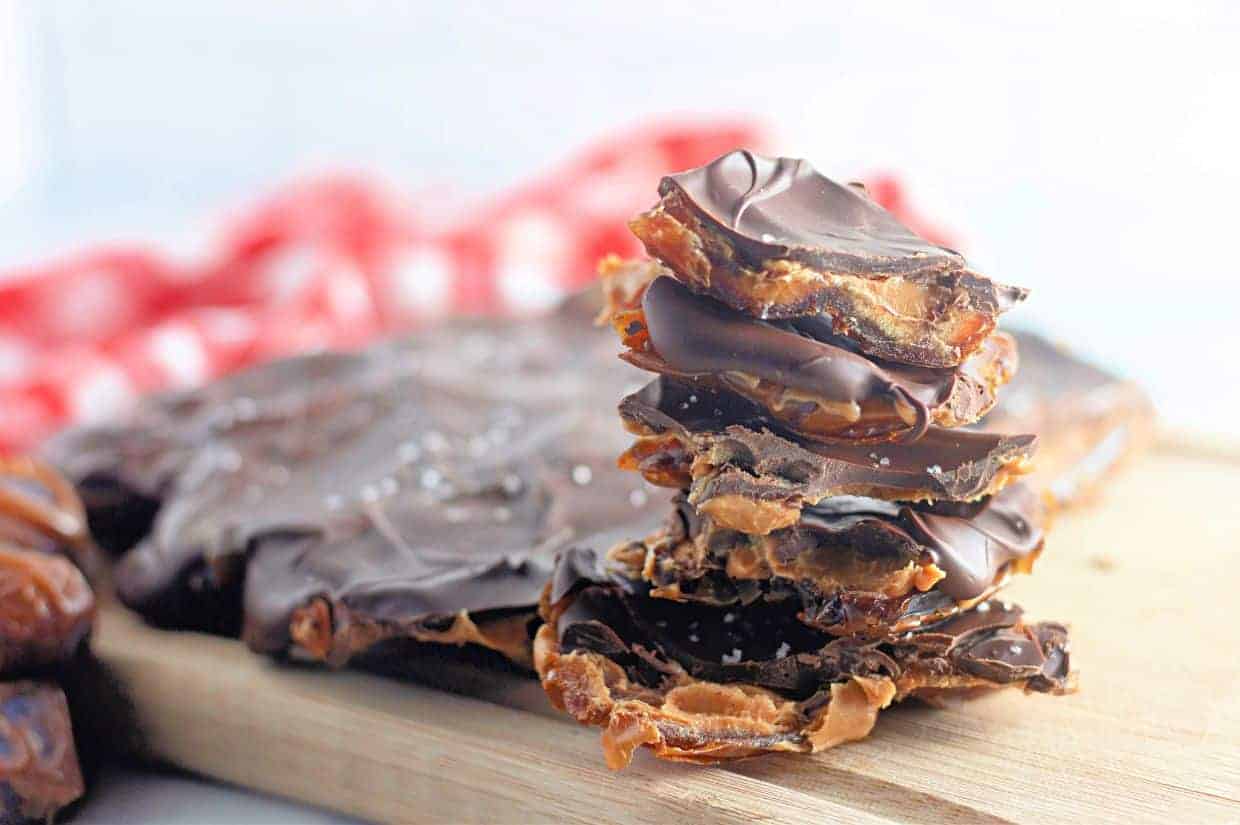 A stack of Peanut Butter and Date Chocolate Bark pieces sits on a wooden board.