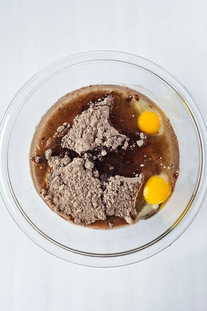 A bowl of brown liquid with eggs and flour.
