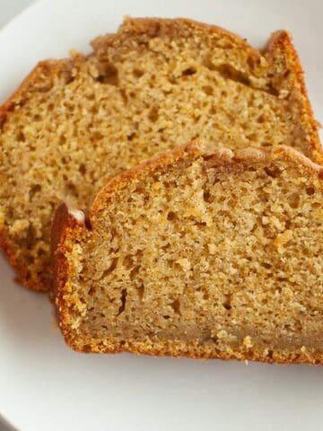 Two slices of Butternut Squash Loaf with Spiced Icing are placed on a white plate, showing a moist and dense texture with a golden-brown crust.