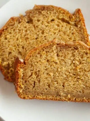 Two slices of Butternut Squash Loaf with Spiced Icing are placed on a white plate, showing a moist and dense texture with a golden-brown crust.