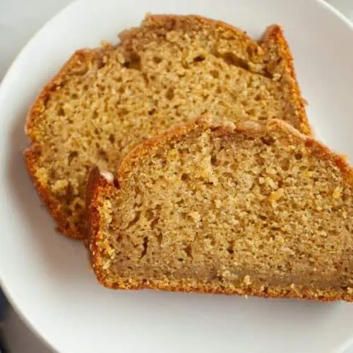 Two slices of Butternut Squash Loaf with Spiced Icing are placed on a white plate, showing a moist and dense texture with a golden-brown crust.