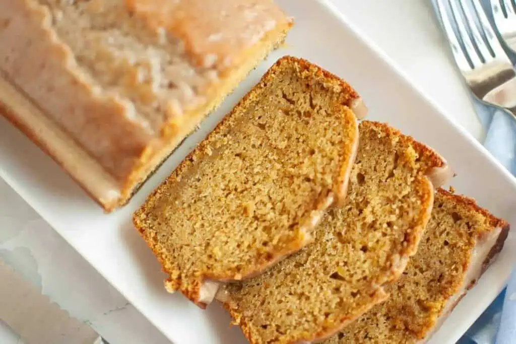 Sliced loaf of glazed bread on a white rectangular plate, with three slices laid out and the remaining loaf beside them.