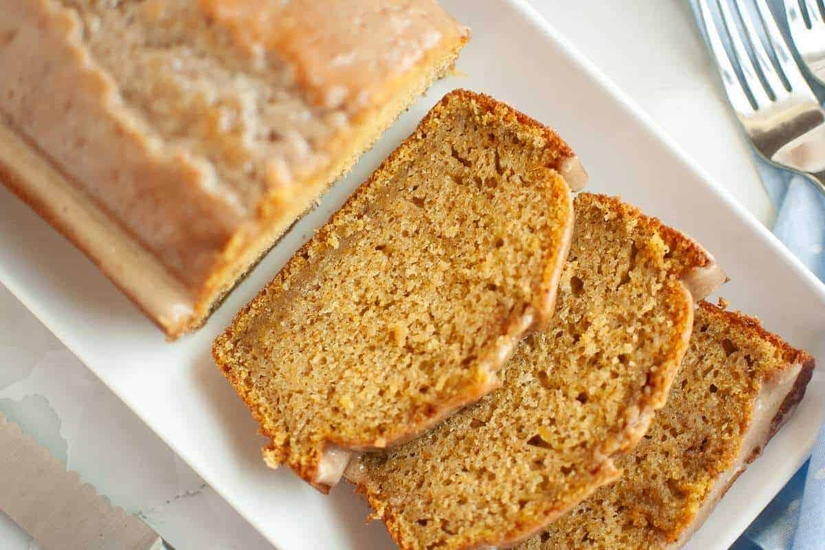 Three slices of Butternut Squash Loaf with Spiced Icing beside the remaining loaf bread on a plate.