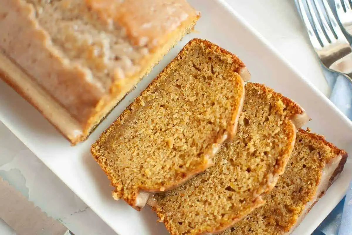 Three slices of Butternut Squash Loaf with Spiced Icing beside the remaining loaf bread on a plate.