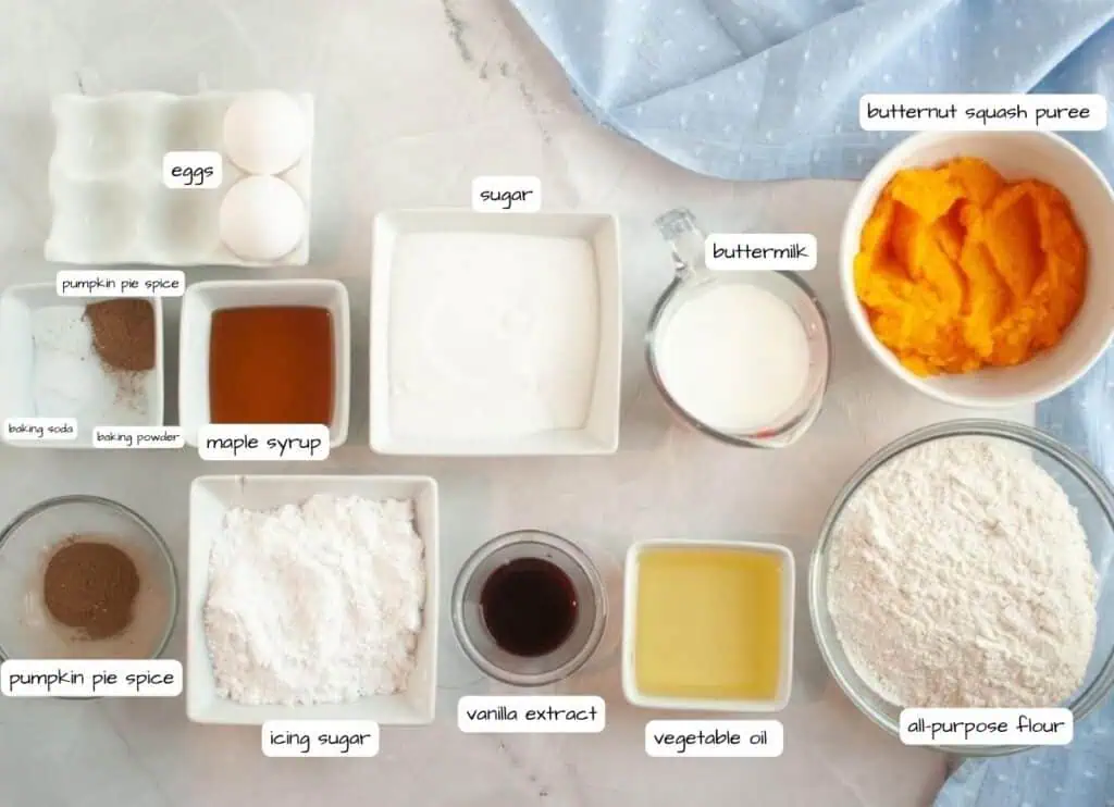 Various baking ingredients including eggs, sugar, buttermilk, butternut squash puree, all-purpose flour, vegetable oil, vanilla extract, icing sugar, maple syrup, pumpkin pie spice, baking soda, and baking powder.