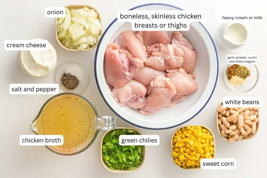 A bowl of raw chicken breasts or thighs surrounded by bowls of chopped onion, cream cheese, chicken broth, green chilies, sweet corn, white beans, seasonings, salt, pepper, and cream.